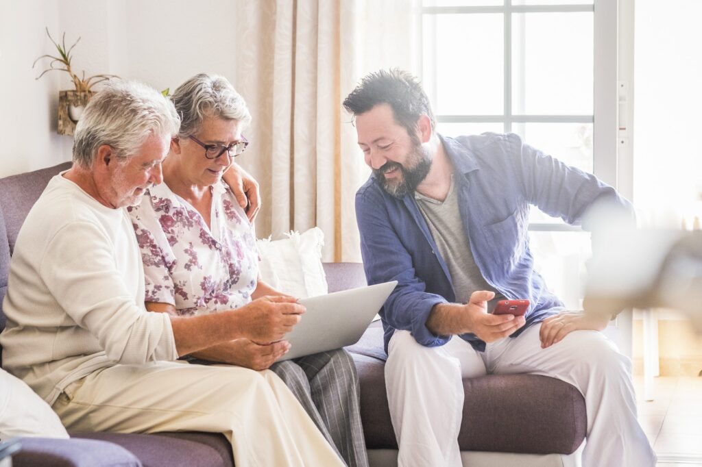 Family sitting together on the sofa using modern device laptop and phone and enjoying connection